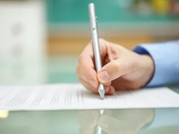 A person writing on paper with a pen.